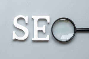 SEO (Search Engine Optimization) text and magnifying glass on gray background