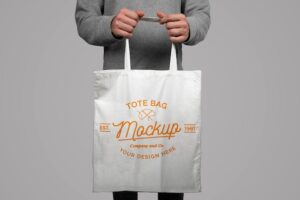 Mockup of model holding a tote bag on a gray background