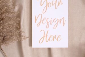 White blank paper card mockup with pampas dry grass on a beige colored textile