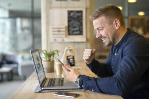 Happy freelancer with tablet and laptop computer in coffee shop