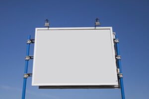 Low angle view of blank hoarding with lights against blue sky
