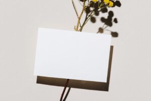 Mockup with blank paper business card and dried yellow flower over beige pastel background