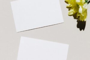 Mockup with blank paper business card and yellow flower over beige pastel background with trendy shadow and sunlight minimal business brand template flat lay top view