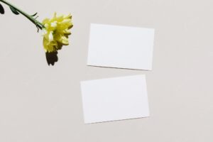 Mockup with blank paper business card and yellow flower over beige pastel background
