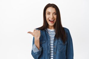 Hey go that way. smiling friendly woman suggest follow this page, pointing finger left and looking excited, inviting people, recommending item, white background