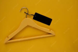 Wooden coat hanger with black paper label isolated on yellow paper background. clothing tag, label b