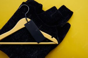 Wooden hanger with black cosy pullover and paper label isolated on yellow paper background. clothing