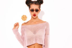 Young beautiful sexy hipster woman with red lips in sunglasses.trendy girl in summer swimwear clothes. eating candy lollipop