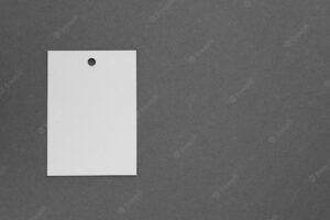 Brand label tag of white color made of cardboard for clothes with little hole in top part placed on left on dark gray background tag mock up copy space