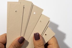 Bunch of blank cardboard rectangular tags with tiny holes in upper part in female hands with shadows falling on white background tag mock up copy space