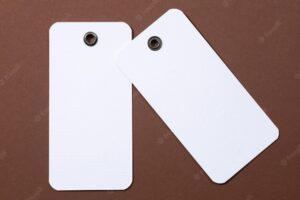 Cardboard blank white colored tags of rectangle shape with tiny holes in upper part for clothes in center on brown background tag mock up copy space