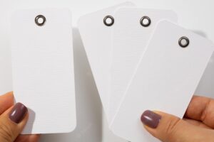Female hands with four cardboard blank white colored tags of rectangle shape with tiny holes in upper part for clothes on white background tag mock up copy space