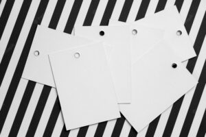 Stack of white cardboard label tags for clothes with little holes in top part of each positioned in center on zebralike white and black background tag mock up copy space