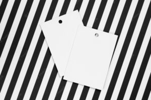Two white label tags made of cardboard for clothes with small holes in top part of each placed in center on white and black background tag mock up copy space