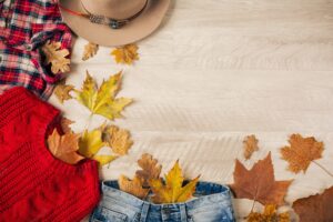 View from above on flat lay of woman style and accessories, red knitted sweater, checkered flannel shirt, denim jeans, hat, autumn fashion trend, traveler outfit