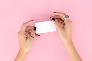 Womans hand with trendy manicure holding business card on pink