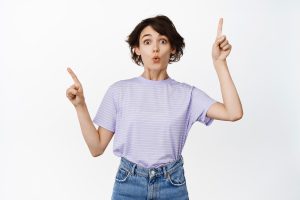 Wow take a look excited young woman with short pixie hairstyle gasp impressed showing two choices few products on sale in shop pointing fingers sideways white background