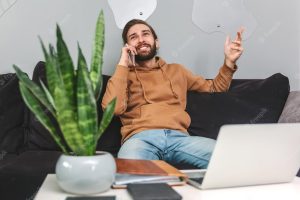 Attractive positive man talking on mobile phone and gesturing while sitting on sofa at home