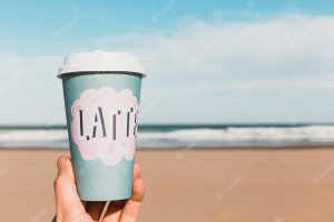 Beach concept with hand holding paper cup