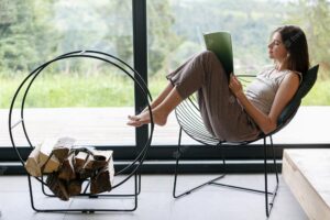 Beautiful stylish woman reading book on chair at firewood at window with view on mountain hills