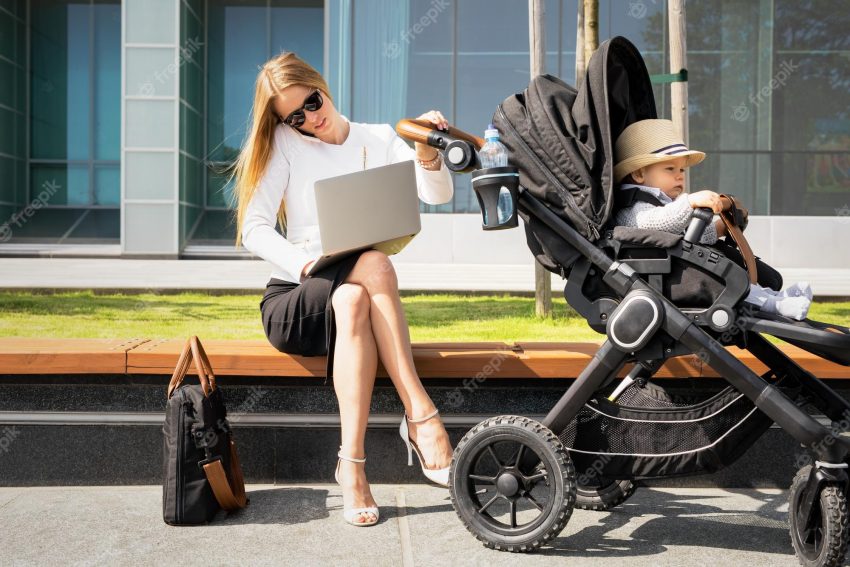 Business woman with child in stroller talking on the phone and working on laptop