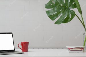 Cropped shot of home office with copy space, laptop, decorations and coffee cup on white table with white wall