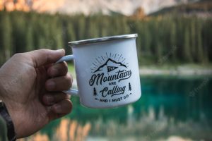 Hand holding a white mug with a blurry mountain landscape as