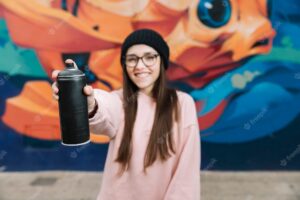 Happy woman holding spray bottle in front in front of graffiti wall