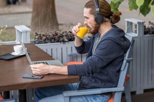 Man enjoying juice at a city terrace while working on laptop