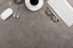 Mouse; keyboard; coffee cup; ear phone; wrist watch on gray background