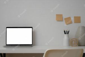 Open laptop computer in minimal workplace with ceramic vase and office supplies