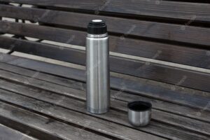 Open steel metal thermos with tea or coffee on a wooden bench.