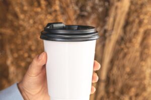 Paper cup with coffee to go on a blurred background of field plants