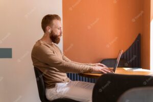 Side view bearded man working on laptop
