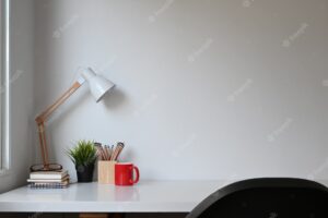 Simple workspace with lamp, plant, coffee cup and copy space on white table.
