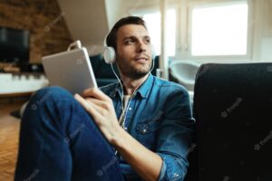 Smiling man  wearing headphones and using touchpad and while relaxing in the living room.