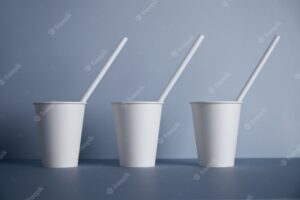 Three take away white paper cups without caps with drinking straws inside presented in center