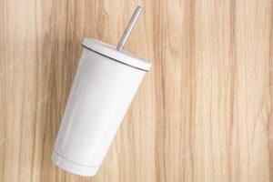 White steel mug with tube on wood background. insulated container for keep your drink.