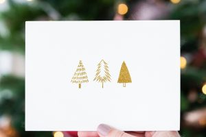 Woman holding a christmas card in front of a christmas tree mockup
