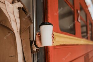 Woman holding a cup of coffee next to train