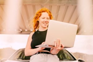Woman working on laptop beside car outdoors