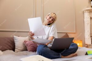Young blonde woman working from home in her bed