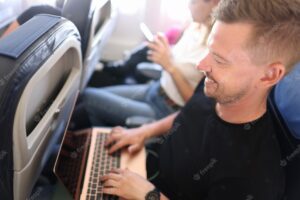 Young man flying in airplane and typing on laptop keyboard