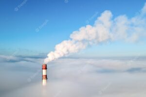 Aerial drone view of thermal station's tube visible above the clouds with smoke coming out. blue and clear sky