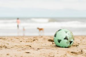 Ball on sand coast and person with dog near water