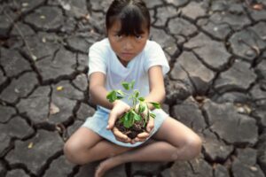 Children siting on crack ground holding young plant. concept save world