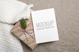 Christmas greeting card mockup with decorated gift box and knitted sweater on linen background