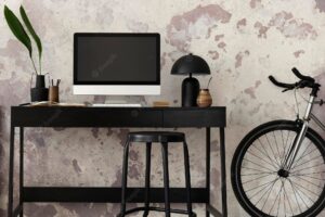 Concrete interior of home office with black desk brown armchair computer screen office accessorieslamp and bicycle rack with personal accessories home decor template