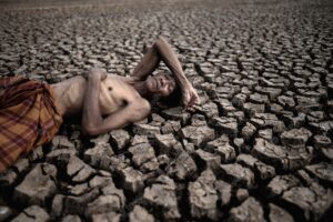 Elderly men lay flat on their hands, on the stomach and forehead, on dry soil, global warming.