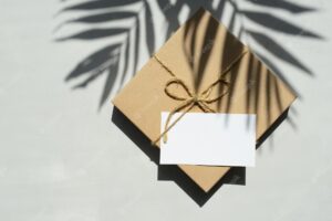 Gift box wrapped in kraft paper with blank greeting card on gray background palm tree leaf shadows